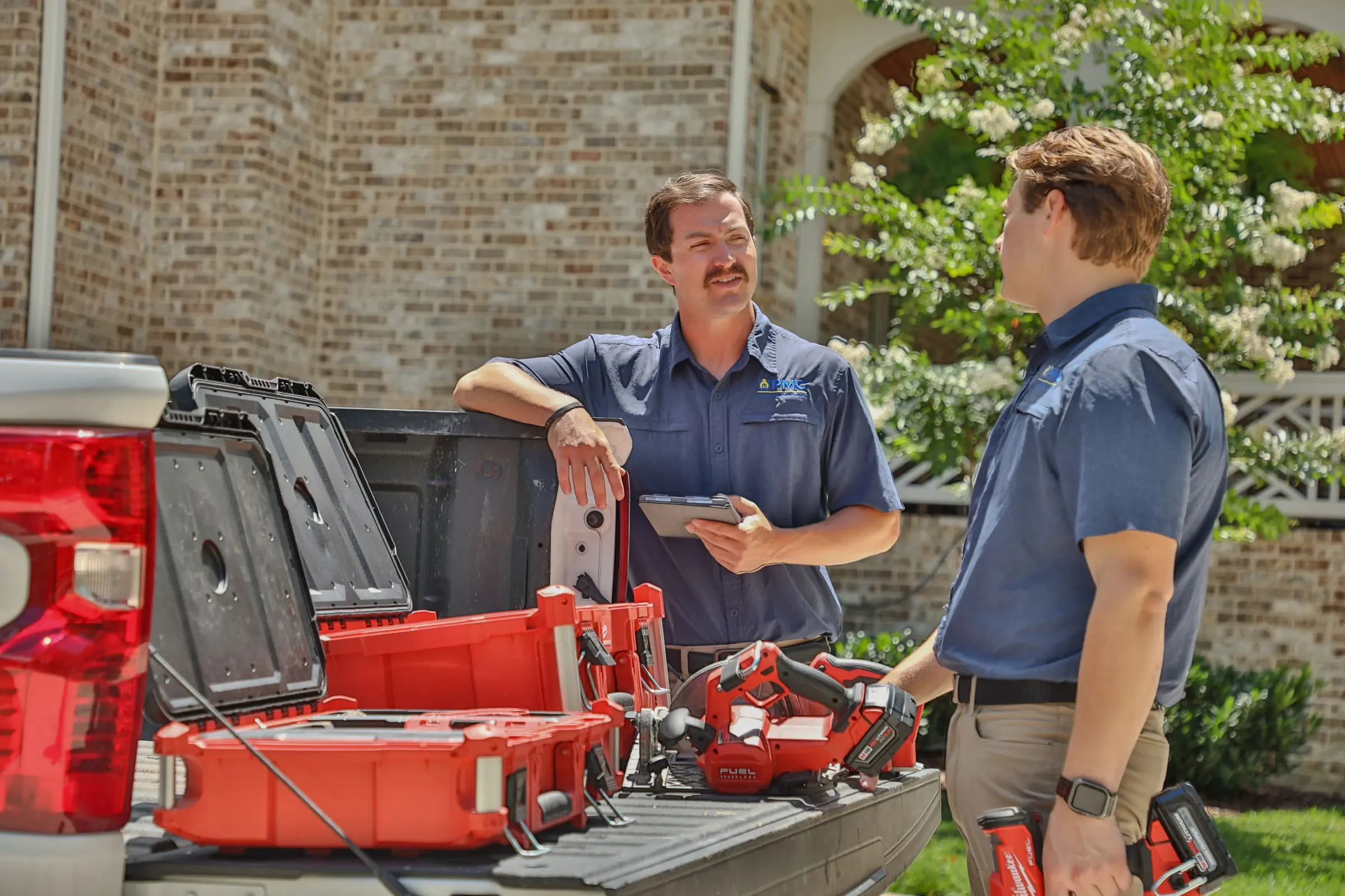 Two PMG technicians talking at the back of the work truck, one holding a tablet